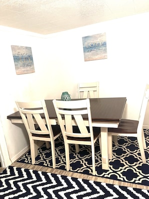 Un coin repas comprenant une table et quatre chaises, un tapis à motifs et deux éléments de décoration murale.