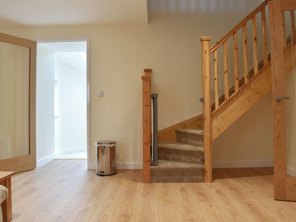 A wooden staircase with carpeted steps leading to a second floor, a trash can, and a door leading to another room.