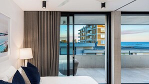 A modern hotel room with a large bed, a view of the sea, and a balcony with a cityscape. - The Arden 7 Coogee New Beachside Ocean View Apt (Coogee)