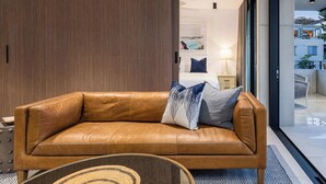 A modern hotel room with a leather sofa, a small round table, and a view of the adjacent room. - The Arden 7 Coogee New Beachside Ocean View Apt (Coogee)
