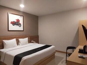 A hotel room with a bed, a desk, a chair, a framed motorcycle picture, and a telephone. - Sukho Hotel (Ciakar)