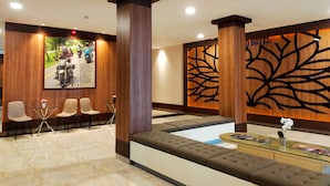 Zona de recepción de hotel con área de descanso, mostrador de recepción y pared con diseño de árbol.