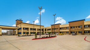 A multi-story hotel with a central courtyard, outdoor parking, and a clear blue sky. - Scottish Inn & Suites Houston Willowbrook (Houston)