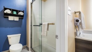 A bathroom with a glass shower enclosure, a toilet, a towel rack, and a hairdryer on the counter. - Scottish Inn & Suites Houston Willowbrook (Houston)