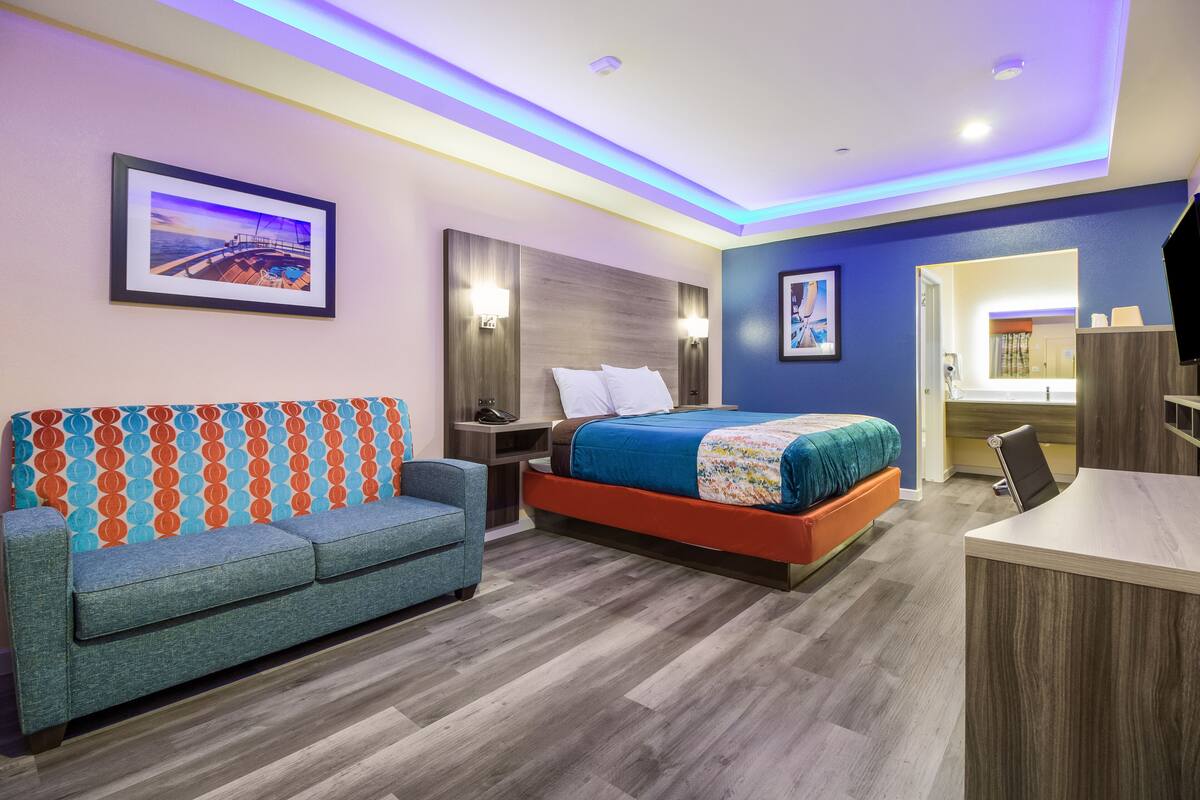Una habitación de hotel moderna con cama, sofá, escritorio y baño visible a través de una puerta abierta.