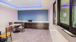 A modern kitchen with dark cabinets, a white countertop, and a blue accent wall. - Scottish Inn & Suites Houston Willowbrook (Houston)