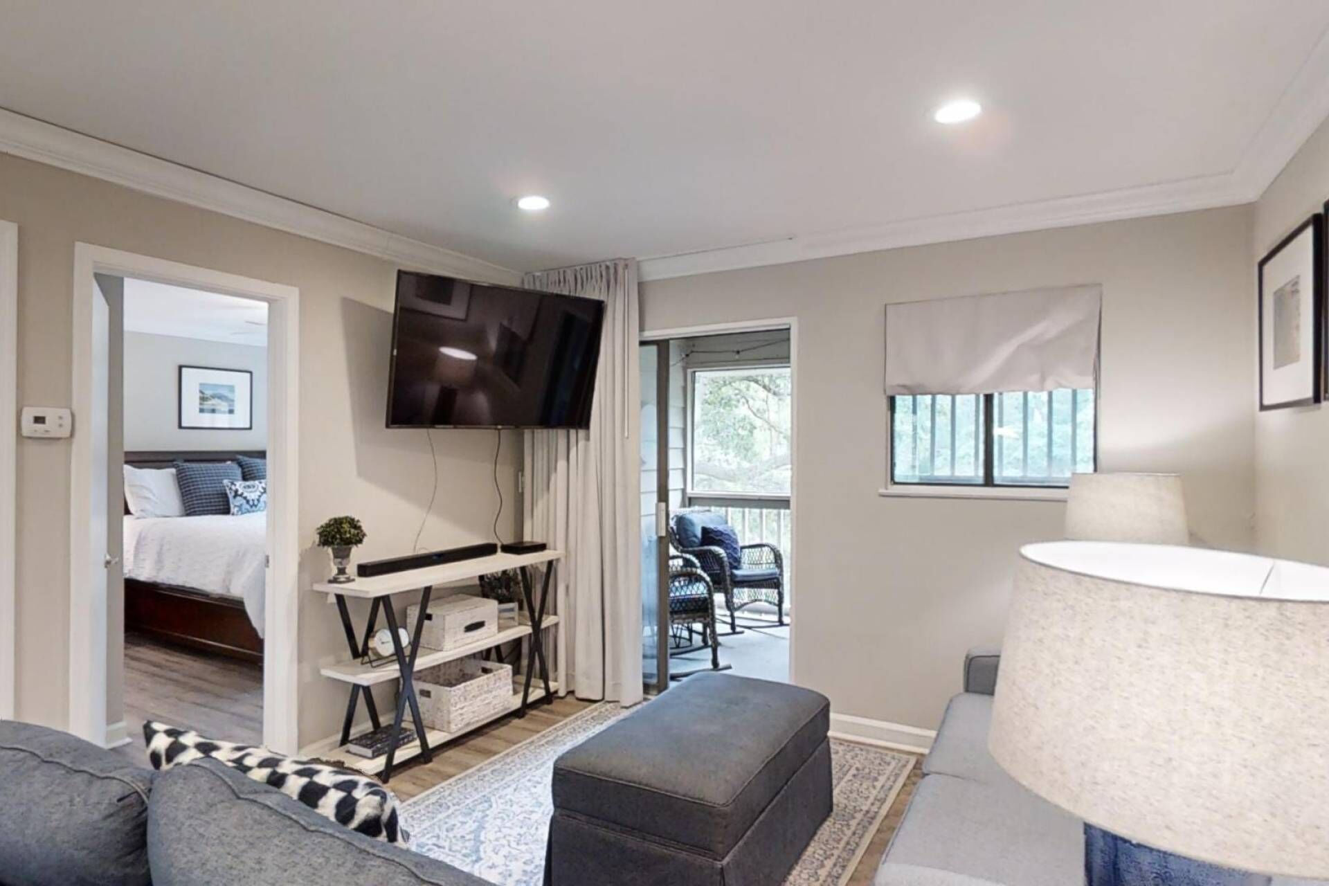 A modern living room with a flat-screen TV, a sofa, a lamp, and a view of the outdoors.