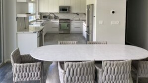 A modern kitchen with white cabinets, a central island, and a dining area with a round table and cushioned chairs.