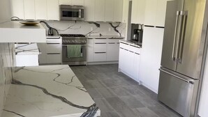 A modern kitchen with white cabinetry, a stainless steel refrigerator, and a marble countertop.