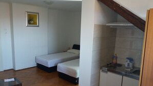 A small, compact room with two single beds, a kitchenette with a sink and stove, and a dining area with a table and chairs. - Apartments Bulic (Split)