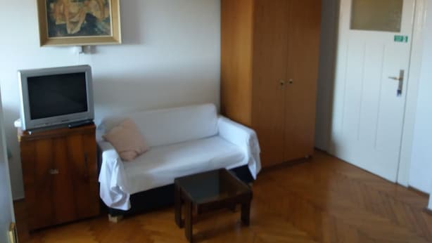 A room with a wooden floor, a white sofa, a small table, a TV on a wooden cabinet, a wardrobe, and a painting on the wall. - Apartments Bulic (Split)