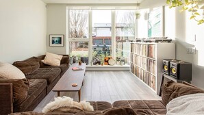 A modern living room with a brown sofa, a wooden coffee table, and a bookshelf filled with books and records. - Stunning Modern Townhome, 4-Bed, 2-Bath, & Patio in the City's Best Location (Vancouver)