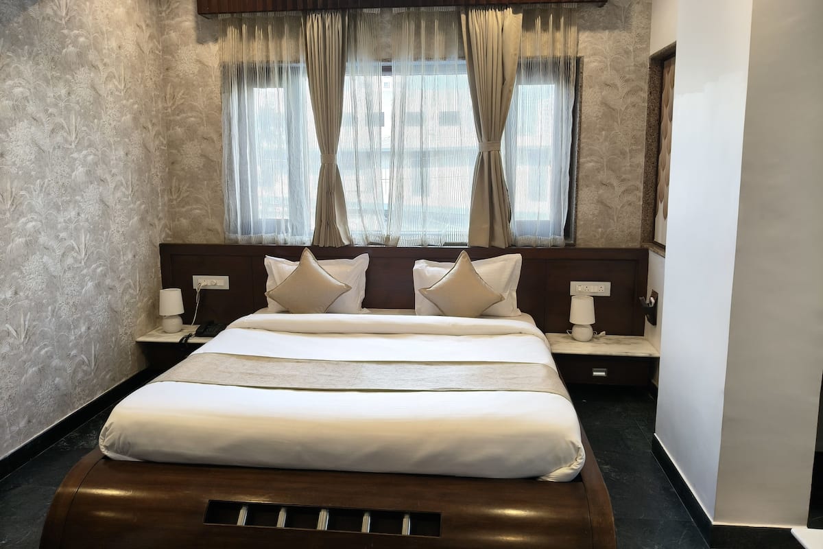 Ein Hotelzimmer mit einem großen Bett, zwei Nachttischen mit Lampen, einem Fenster mit durchscheinenden Vorhängen und einer strukturierten Wand.