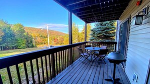Eine Holzterrasse mit Tisch und Stühlen, mit Blick auf ein bewaldetes Gebiet und Hügel.