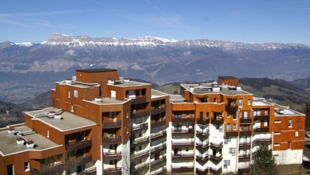 A modern apartment building with multiple balconies and a view of snow-capped mountains in the background.