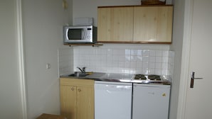 A compact kitchen with a microwave, sink, dishwasher, and a small wooden table.
