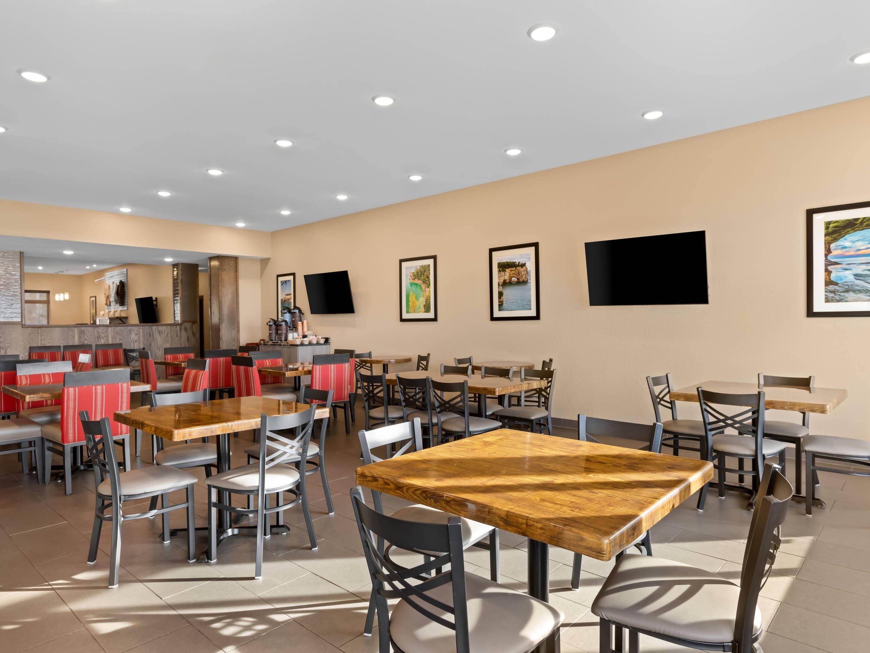 A spacious dining area with multiple tables and chairs, a counter with a coffee machine, and framed pictures on the walls.