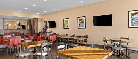 A spacious dining area with multiple tables and chairs, a counter with a coffee machine, and framed pictures on the walls.