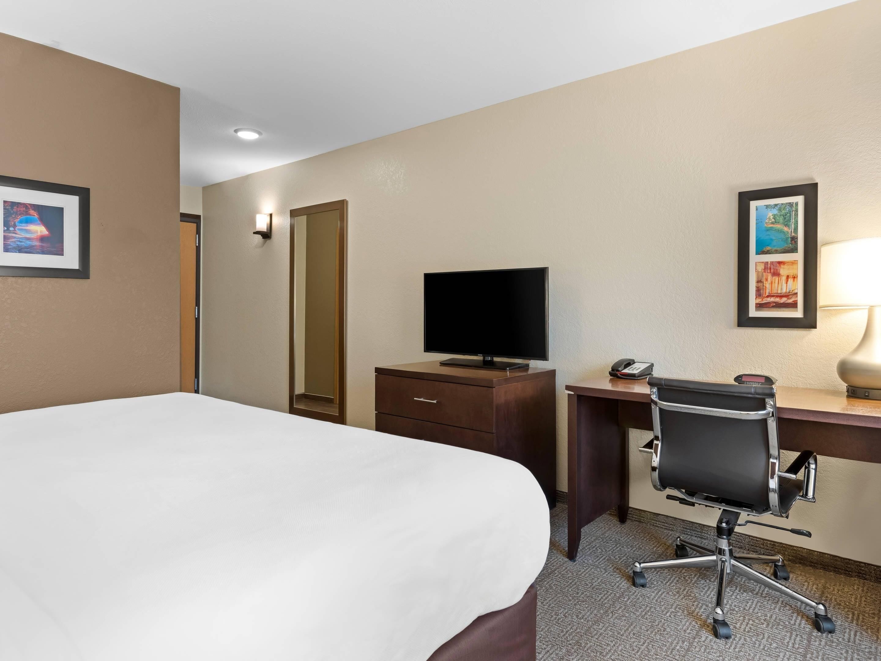 A hotel room with a large bed, a desk with a computer, a chair, a TV, and a phone.