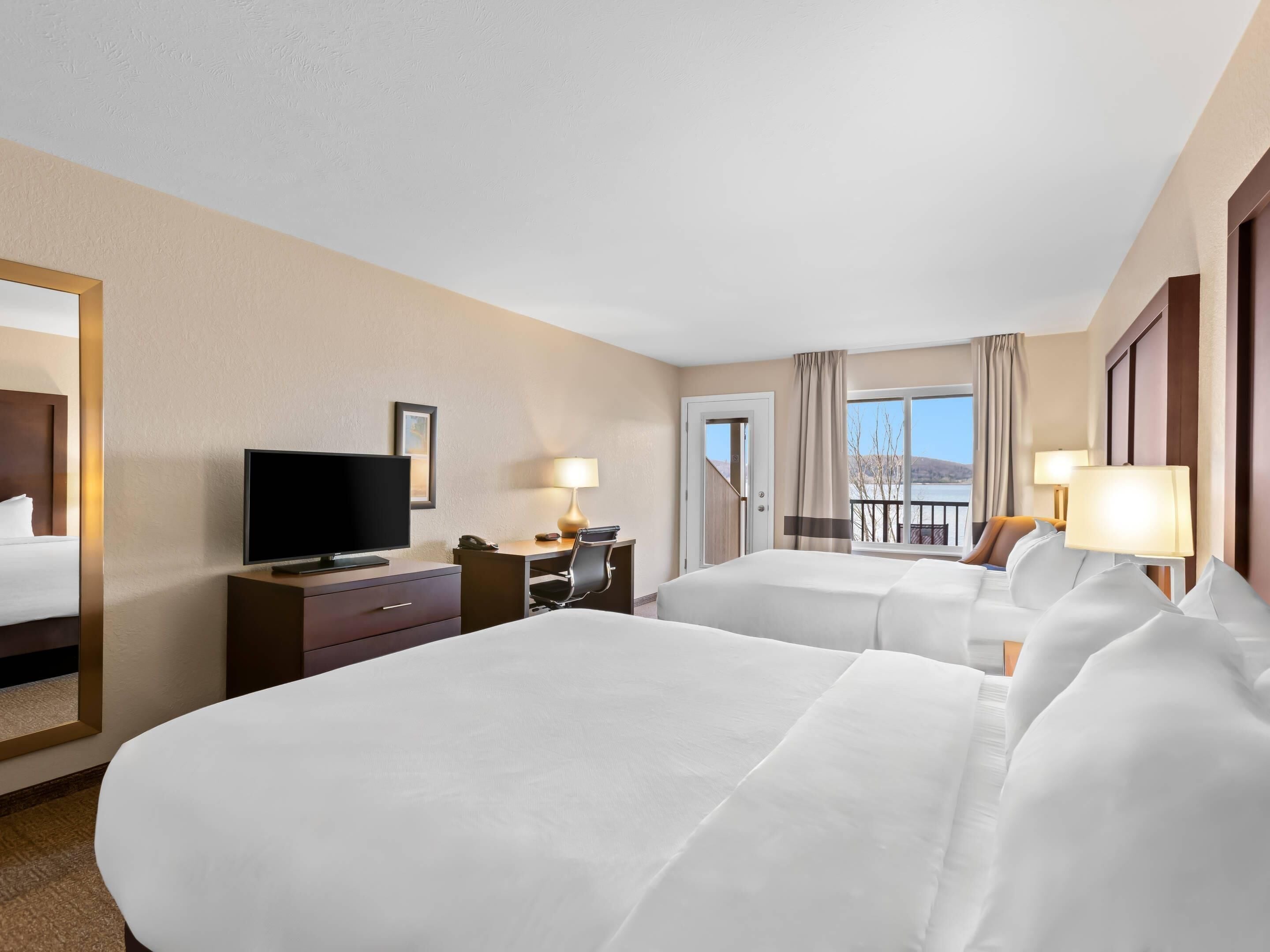 A hotel room with two beds, a TV, a desk, and a view of the outdoors.
