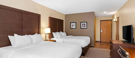 A hotel room with two beds, a desk, a television, and framed pictures on the wall.