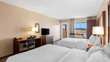 A hotel room with two beds, a desk with a TV, and a balcony with a view.
