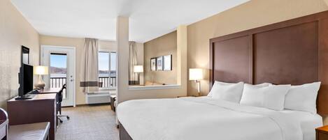 A hotel room with a large bed, a desk with a chair, a TV, and a window with curtains.