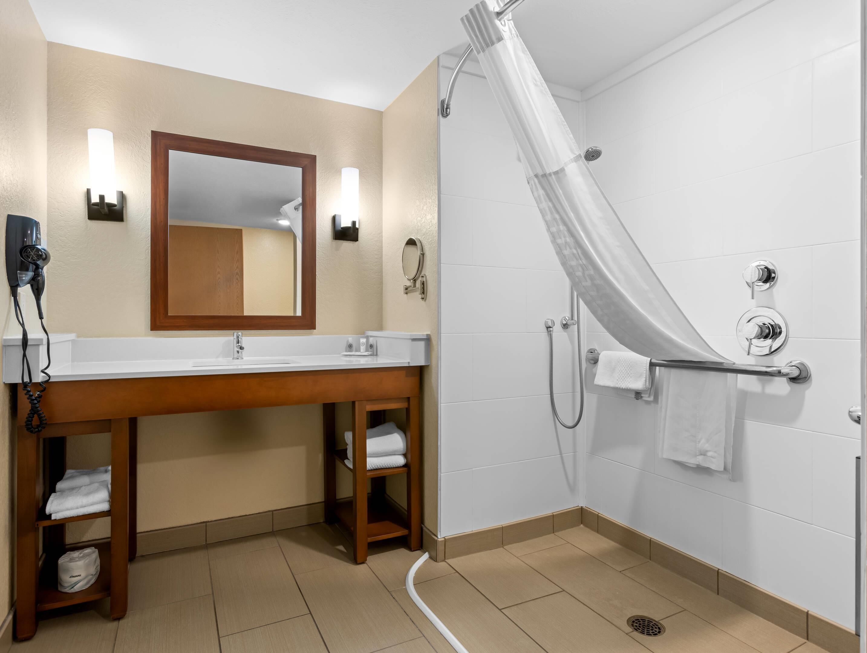 A bathroom with a wooden vanity, a large mirror, a shower with a curved glass door, and a towel rack.