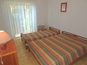 Una habitación con dos camas, una mesita de noche con lámpara y una ventana con cortinas.