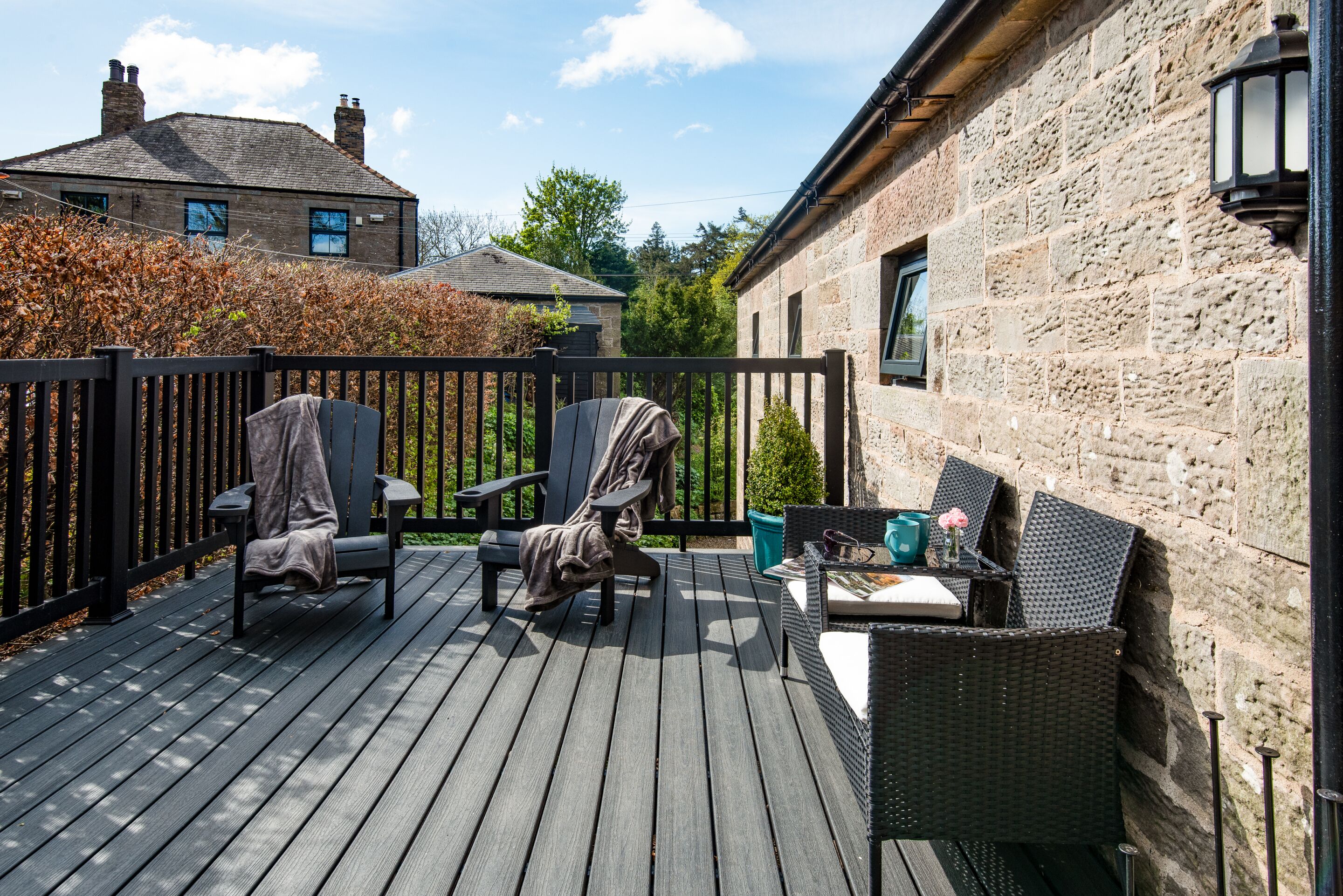 A wooden deck with outdoor furniture, including chairs and a table, adjacent to a stone building.