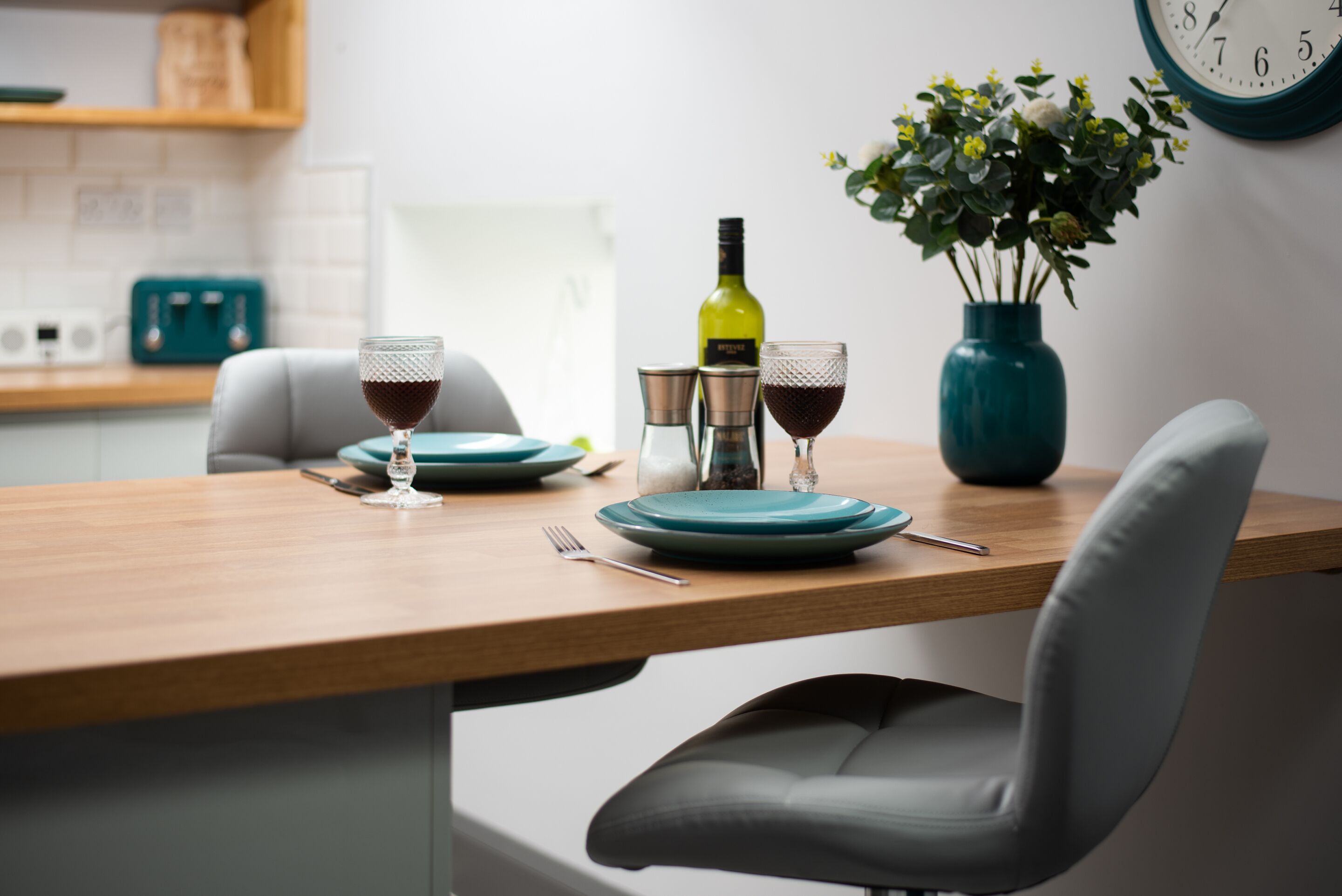 A dining table set with plates, glasses, a bottle, and a vase with flowers.