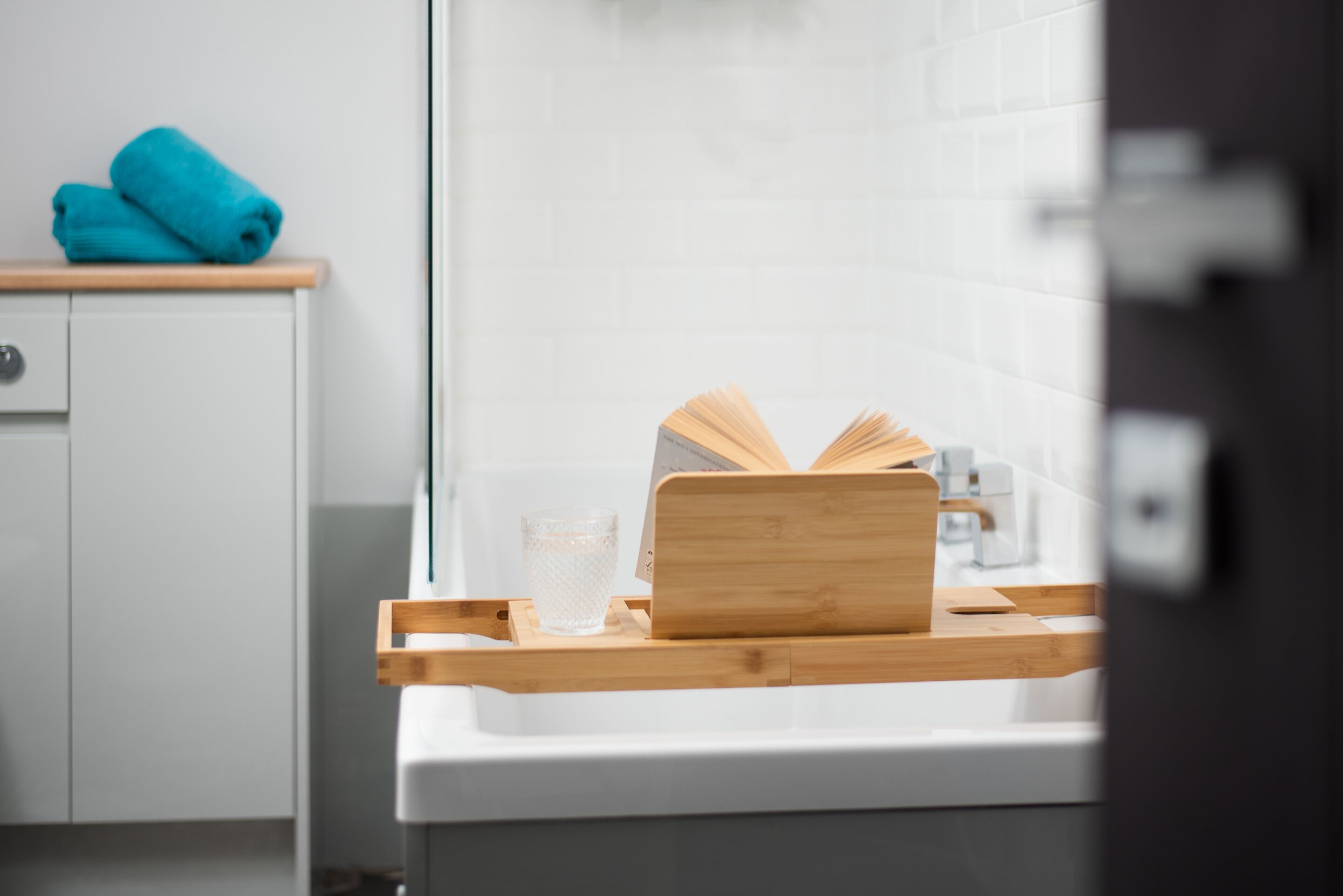 A bathroom with a white sink, a wooden tray, a book, and a glass of water.