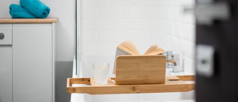 A bathroom with a white sink, a wooden tray, a book, and a glass of water.
