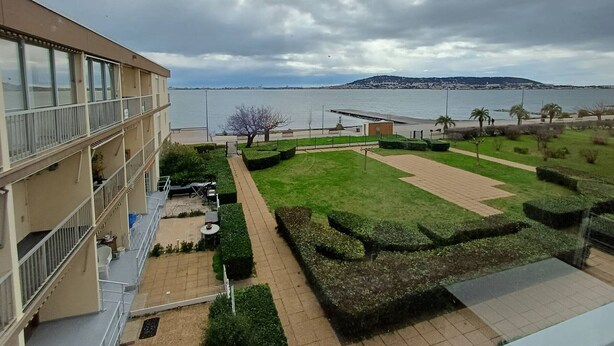 A view of a building with a balcony overlooking a landscaped area with a body of water in the background.