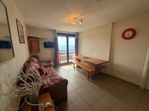 Una sala de estar con un sofá, una mesa de madera, un televisor montado en la pared y un balcón con vistas.
