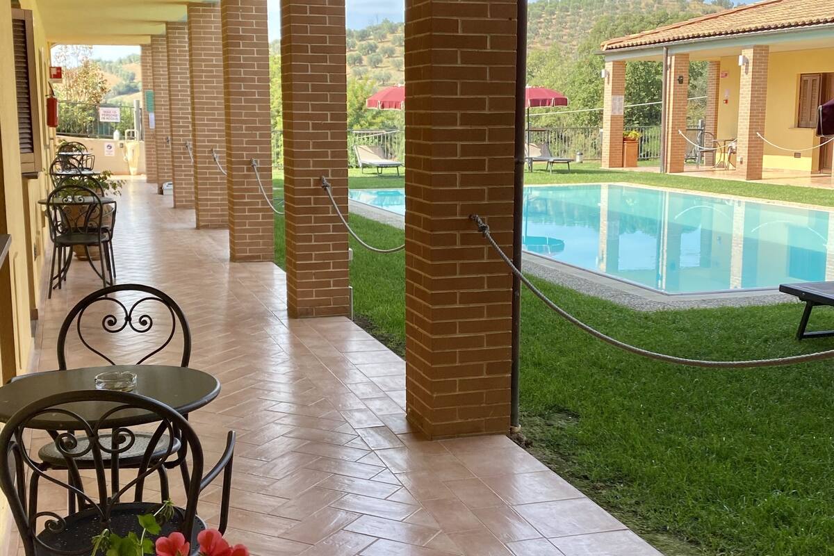 Un espace extérieur abrité comprenant une piscine, des piliers en briques et une table avec des chaises.