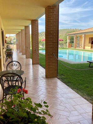 Ein überdachter Außenbereich mit Pool, Ziegelstützen und einem Tisch mit Stühlen.