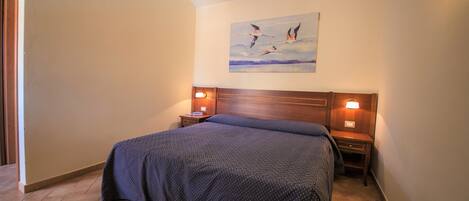 A bedroom with a large bed, two bedside tables with lamps, a wooden headboard, and a painting on the wall.