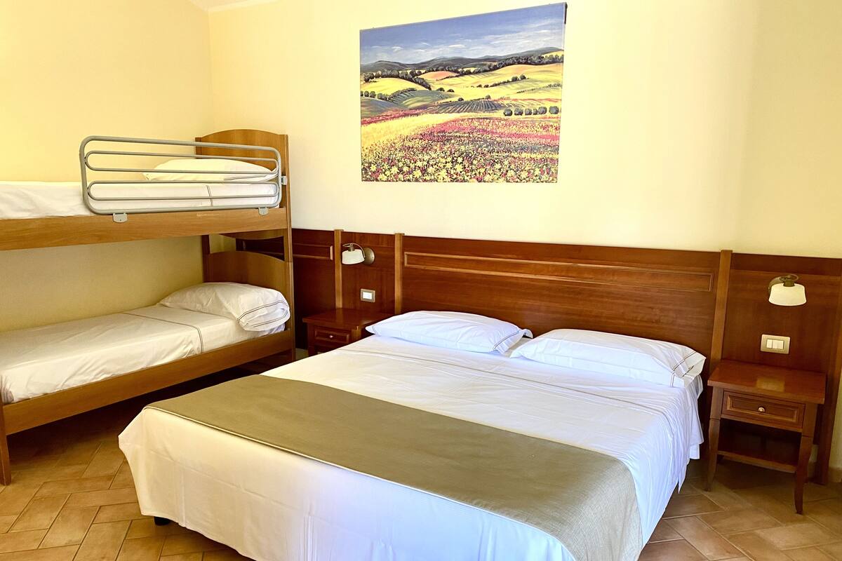 Une chambre avec un lit superposé, un lit simple, une table de chevet et un tableau représentant un paysage.