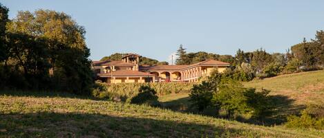 Un edificio grande de varios pisos con un estilo arquitectónico tradicional, rodeado de un paisaje con césped y árboles.