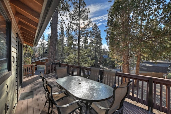 A covered outdoor deck with a table and chairs, surrounded by tall trees.