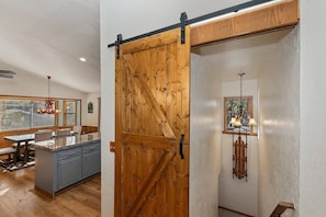 A room with a sliding barn door, a kitchen with grey cabinets, and a dining area with a table and chairs.