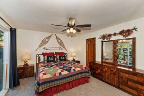 A bedroom with a large bed, a ceiling fan, a wooden dresser, and a mirror reflecting a view.