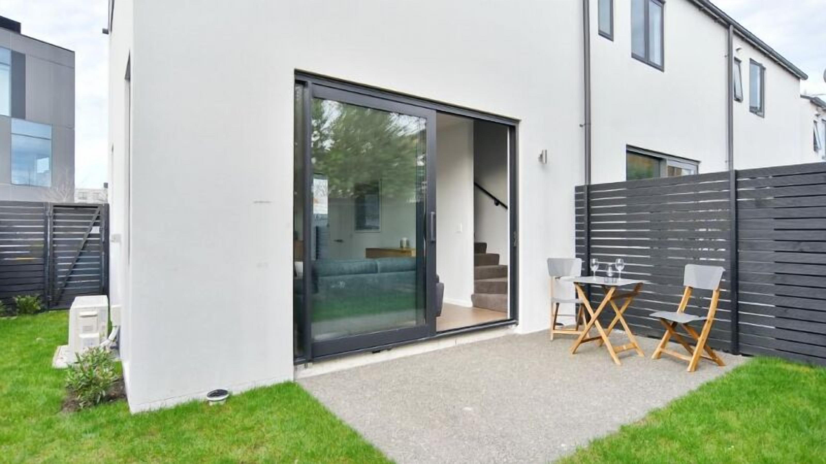 Une maison moderne dotée d’une porte-fenêtre coulissante qui donne sur un patio couvert aménagé avec des meubles d’extérieur.