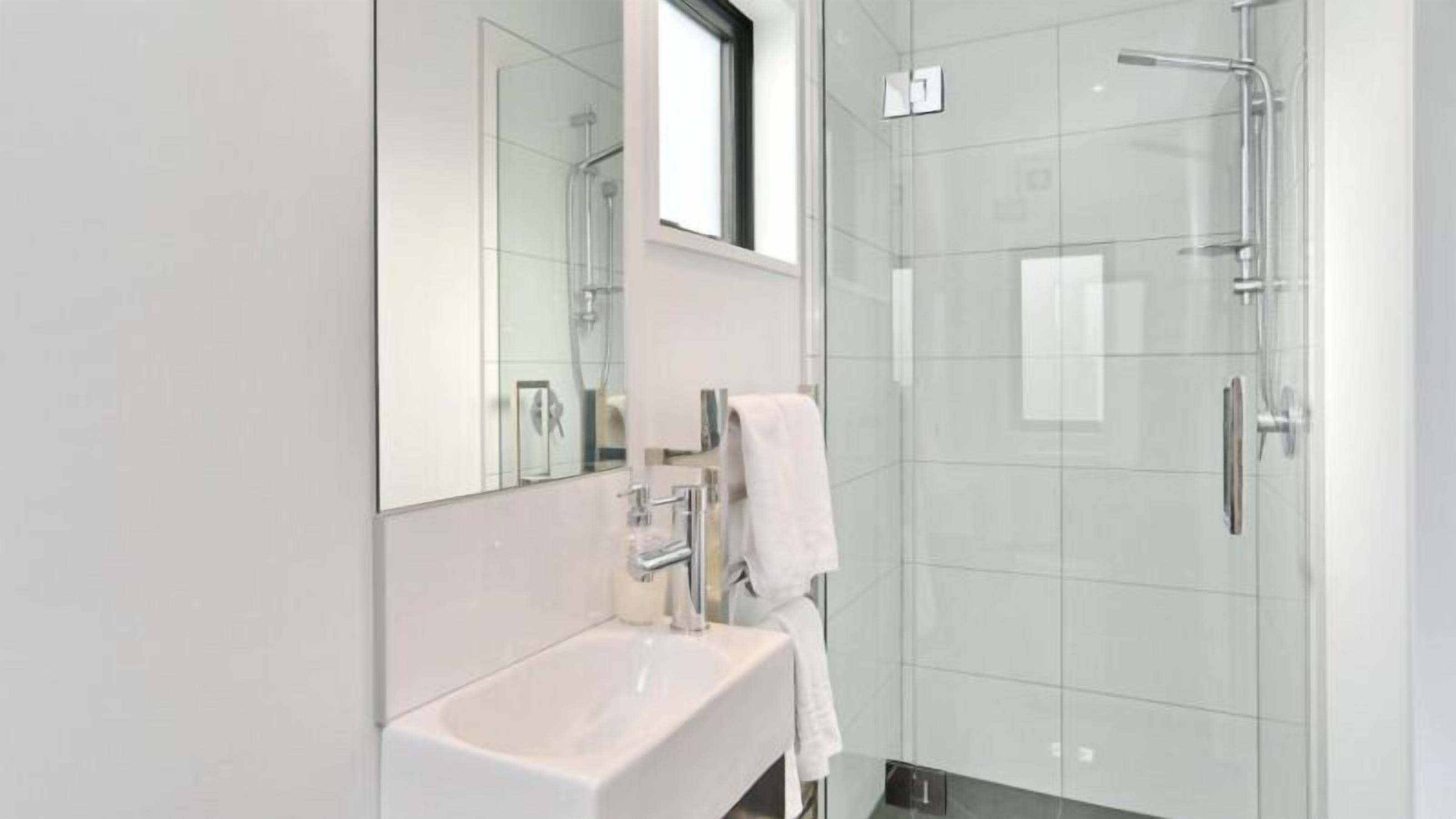 A modern bathroom with a glass shower enclosure, a white sink, and a mirror above the sink.