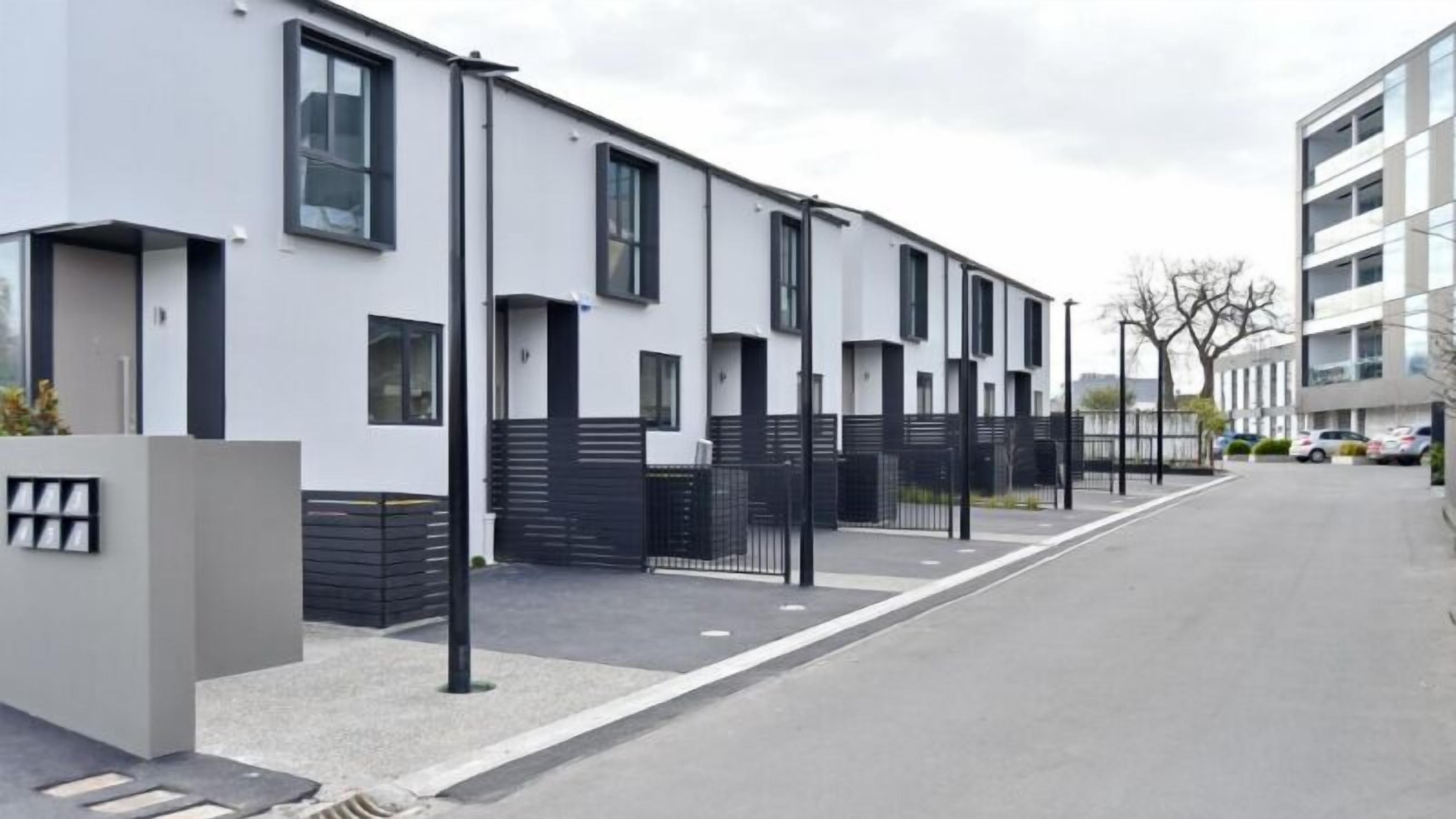 En modern bostadsbyggnad med en stilren och minimalistisk design, som kännetecknas av en rad likadana fönster och en grind vid entrén.