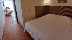 A bedroom with a large bed, a wooden headboard, a bedside table with a lamp, and a wall-mounted shelf.