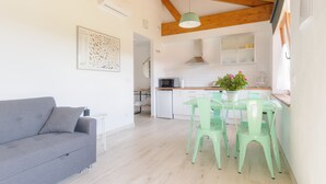 A modern kitchen with wooden beams, a dining table with chairs, and a grey sofa in a bright living area.