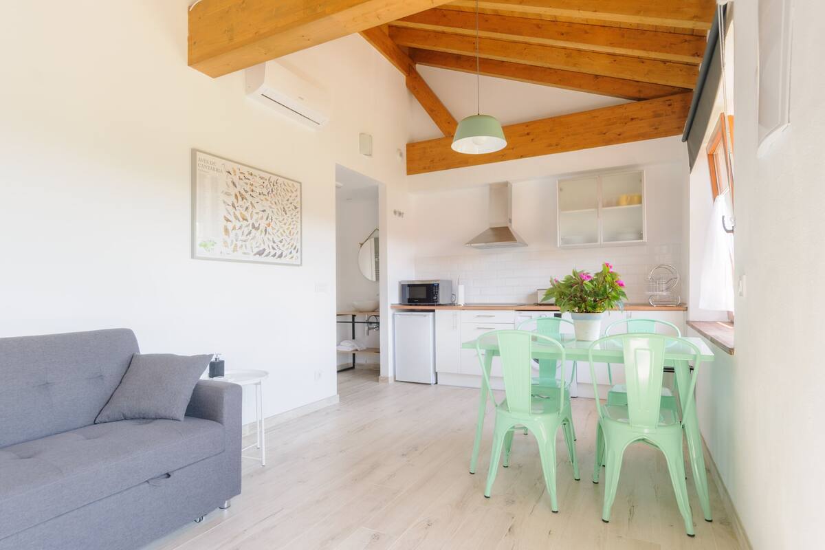 A modern kitchen with a dining area, a grey sofa, and a ceiling with exposed wooden beams.