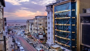 Una strada cittadina con edifici moderni, una strada trafficata e vista sul mare in lontananza.